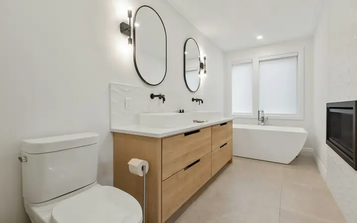 Renovated bathroom with a wood vanity, round mirrors and freestanding tub