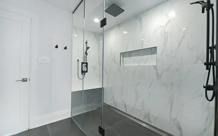 Walk-in glass shower with marble-look tile and a niche