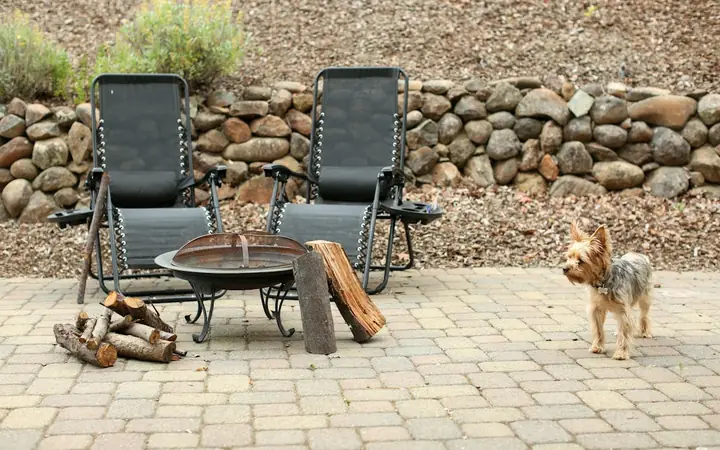 Paver patio with a fire pit and lounge chairs in front of a stone wall