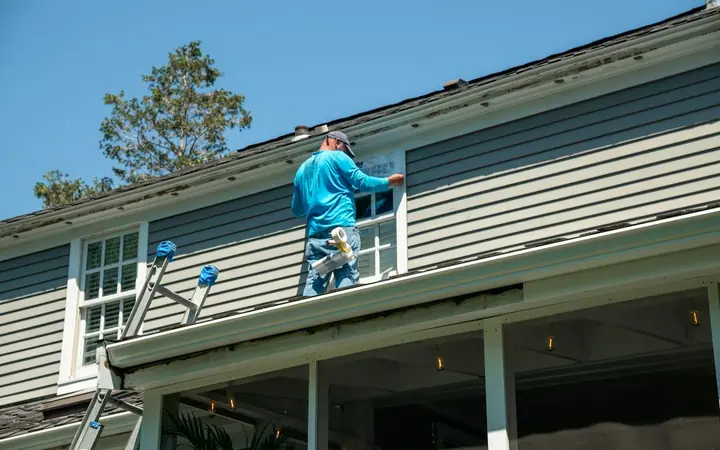 Painter on a ladder working on a house's siding