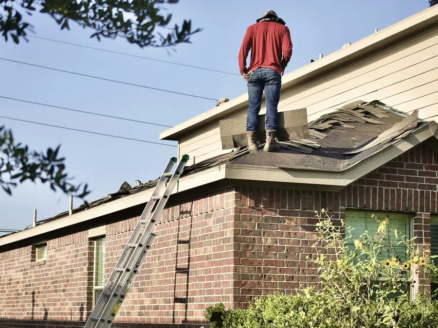 Roofer inspecting the roof of a brick house, with a ladder at the eave
